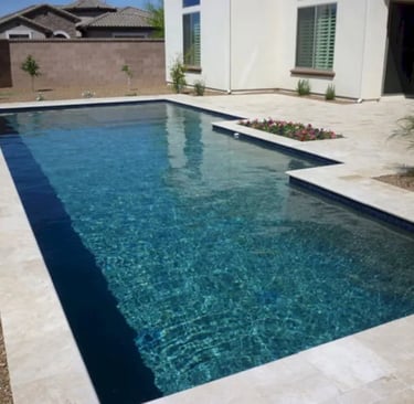 Geometric pool with deep blue water and light stone tiles set against a modern backyard.