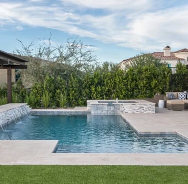 Modern stepped pool with light blue water and pale stone tiling, featuring a waterfall edge