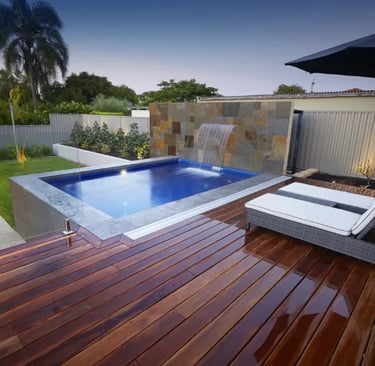 Raised plunge pool with waterfall, deep blue water and grey stone tiles