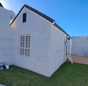 Professional house painter on a ladder applying white paint to a residential home exterior wall.