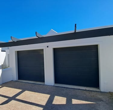 Modern white double garage with dark grey sectional doors and a black wooden pergola.