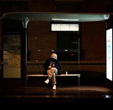 Homme penché sur son téléphone, assis à un arrêt de bus la nuit.