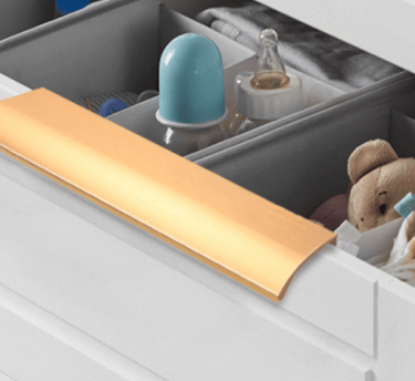 Gold flush cabinet handle on a baby nursery drawer – sleek hardware for organized nursery storage.