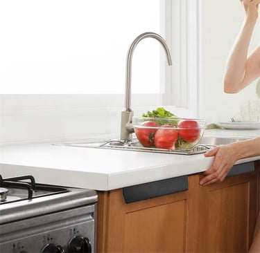 Stainless steel faucet over kitchen sink with fresh tomatoes and lettuce, person adjusting light countertop nearby