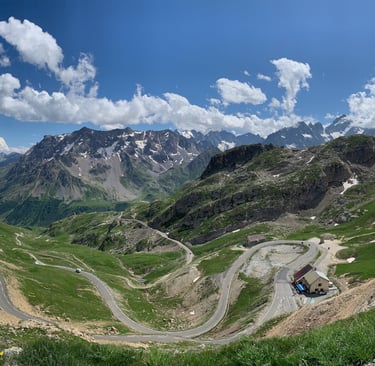 Kurvenreiche Passstrasse durch die französischen Alpen mit grünen Tälern und schneebedeckten Gipfel