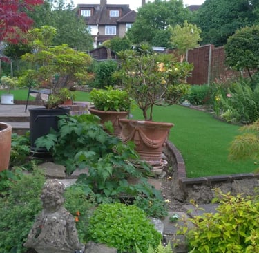 A lush backyard garden featuring terra cotta pots, green lawn, and stone statues for landscaping.