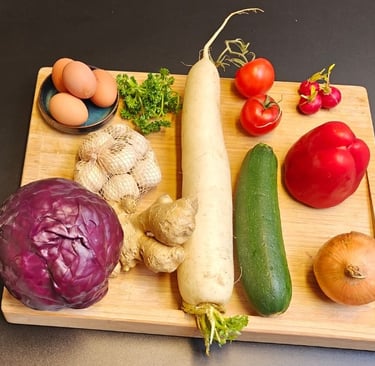 A variety of fresh vegetables including red cabbage, daikon radish, courgette, tomatoes, ginger and red pepper arranged.