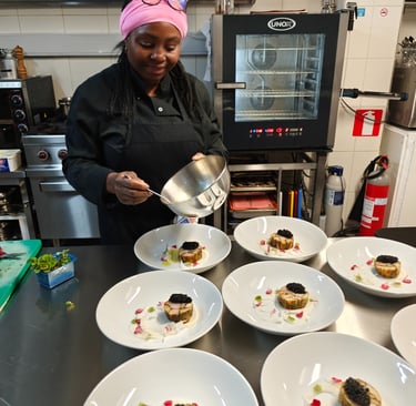 Chef Viviane spooning sauce over multiple fine dining plates lined up on a professional kitchen pass at klavertje vier.