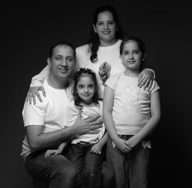 Black and white studio portrait of a smiling Indian family of four posing against a dark background.