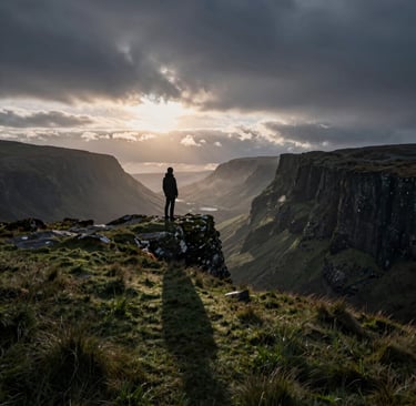 A hiker stands on a mossy cliff edge overlooking a dramatic mountain valley at sunset under cloudy skies.