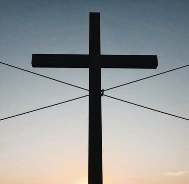 A silhouette of a large Christian cross against a blue and orange sunset sky.