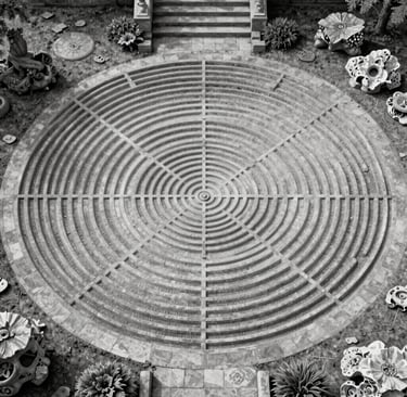 Aerial view of a circular stone meditation labyrinth in a black and white garden setting.