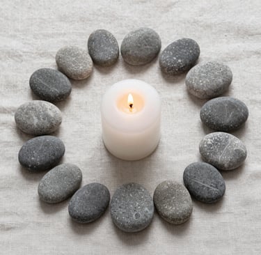 A lit white pillar candle centered within a circle of smooth grey zen stones on beige linen.