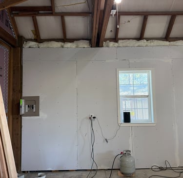 Interior garage renovation showing newly installed drywall, window, and electrical panel.