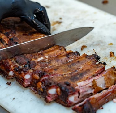 Chef in black gloves slicing smoked BBQ pork ribs on a white cutting board.