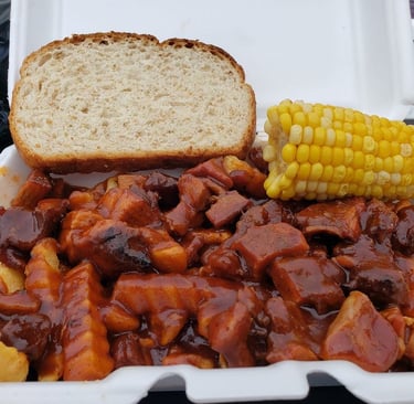 Smothered BBQ turkey fries with corn on the cob and a slice of bread in a takeout container.