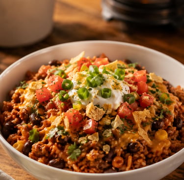 A bowl of hearty taco casserole topped with sour cream, tomatoes, and green onions on a rustic table.