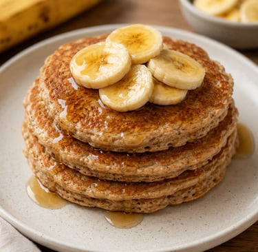 Stack of fluffy whole wheat banana pancakes topped with fresh fruit slices and maple syrup on a plate.