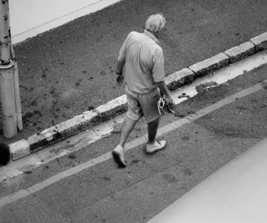 Black-and-white photo of a man walking along a city curb, from Martin Osner’s “On the Move” collection.