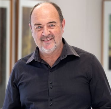 Portrait of Martin Osner, South African photographic artist and painter, smiling in a fine art gallery setting