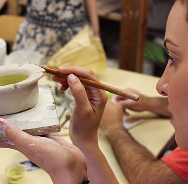 a woman is painting a clay potted with a brush