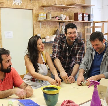 a group of people sitting around a table making pottery