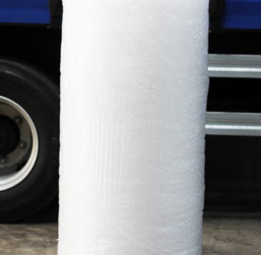 Rolo de plástico bolha grande, ao fundo um caminhão de entregas.