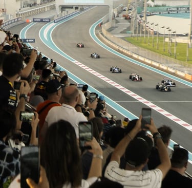 "Fans crowd the grandstand and hold up phones as Formula 1 cars race down the Yas Marina Circuit tra