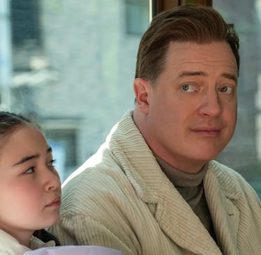 Brendan Fraser sitting beside a young girl, glancing over his shoulder with a subtle expression — sc