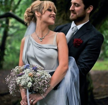 Bride in grey silk dress holding flowers in side embrace with smiling groom