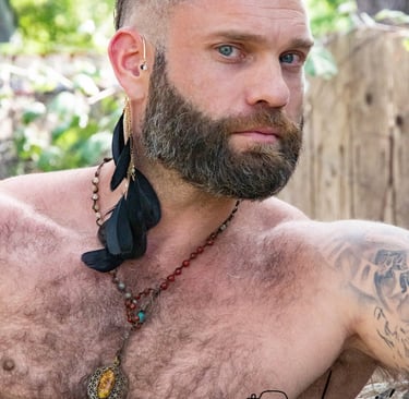 outdoor portrait of shirtless masseuse with a trimmed beard and hairy chest looking intrigued