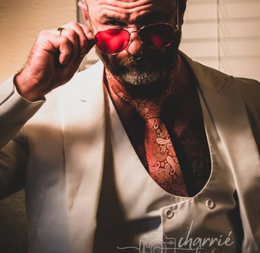 dapper bearded man dressed in formal clothing in low light staring intently over his glasses