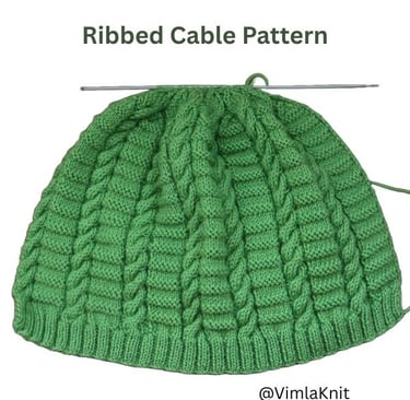 Green knitted beanie in progress, showcasing the detailed cable pattern and ribbed brim on a knitting needle.