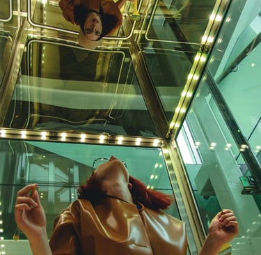 A woman on an elevator looks up at her reflection on the mirrored ceiling panel