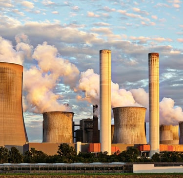 An industrial power plant with multiple cooling towers and smokestacks emitting white smoke into the