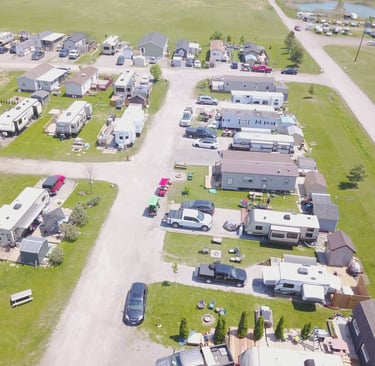 Aerial view of a sunny RV park and campground featuring mobile homes, campers, and parked cars.