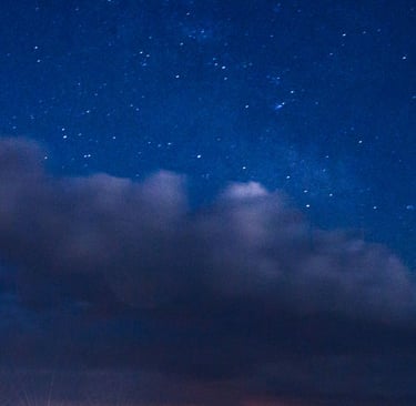 A glowing lighthouse under a starry night sky with a meteor and clouds over the ocean.