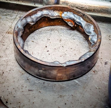 A metal bearing race with weld beads on the inner diameter for removal on a steel workbench.