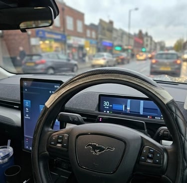 Interior view of a Ford Mustang Mach-E dashboard showing the steering wheel and digital displays in city traffic.