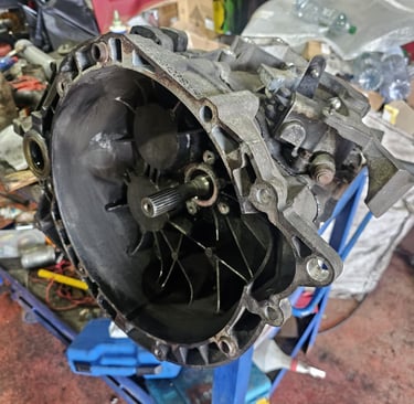 A used manual transmission gearbox housing on a blue stand in an automotive repair shop.