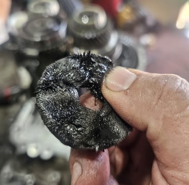 A mechanic holding a magnetic drain plug covered in metal shavings from a vehicle transmission.