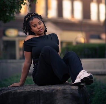 Mujer sentada en una roca al atardecer con edificios urbanos de fondo