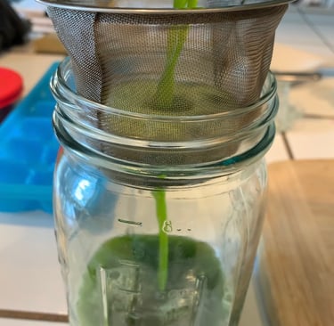 a bright green herbal juice being poured through a strainer into a clear glass jar