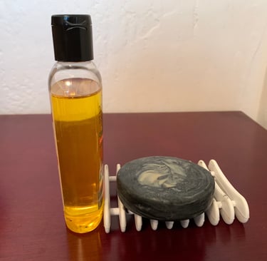 A bottle of golden colored oil next to a bar of round black soap