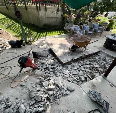 A jack hammer leaning against the side of a patio with concrete that was recently broken up