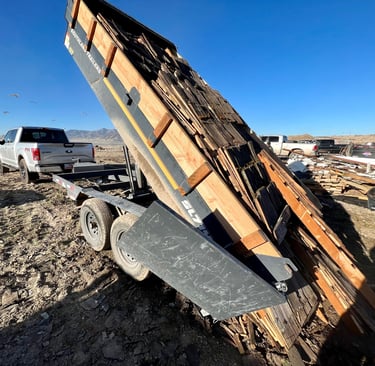 a truck with a dump trailer extended up, dumping a load of roofing debris 