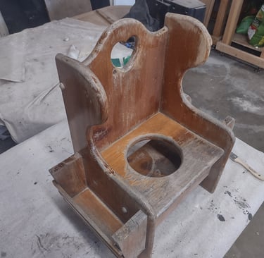 Vintage wooden potty chair with a worn finish undergoing restoration in a workshop setting.
