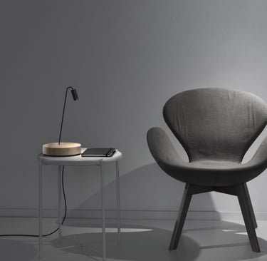 Lámpara de sobremesa con base circular junto a butaca en ambiente de lectura moderno