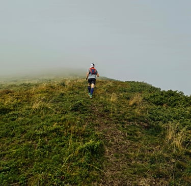 a man hiking on a misty hill wearing a backpack using hiking poles