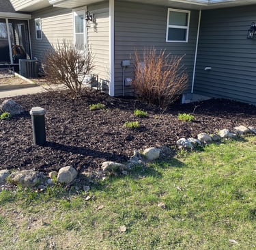 Professional residential landscaping with fresh mulch, trimmed shrubs, and natural stone edging